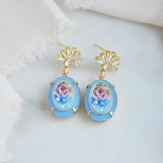 "Cameo Earrings // Flower Earrings // Vintage Earrings // Blue Earrings // Floral Earrings // Art Deco Earrings // Retro Earrings // Boho Bridal Earrings // Oval Earrings  These unique blue cameo earrings blend the beauty of the past with a modern twist for the modern bride. The oval earrings feature matte blue and pink floral motifs surrounded by a golden frame adding a touch of vintage retro style. The fan shaped earring posts are embellished with cubic zirconia and plated with gold. Whether searching for unique wedding earrings or something blue for your next special occasion your beautiful art deco earrings will arrive suitably gift wrapped ready for gift giving. Measurements: The length of the romantic floral cameo earrings hang approx. 1.5\" long Metals: Gold plated 925 sterling silv Elegant Light Blue Flower Earrings, Handmade Formal Drop Flower Earrings, Handmade Flower Drop Earrings For Formal Occasions, Elegant Blue Drop Clip-on Earrings, Blue Drop Flower Earrings, Blue Flower-shaped Formal Jewelry, Blue Drop Flower Earrings With Ear Wire, Elegant Blue Earrings For Gift, Delicate Blue Flower Earrings