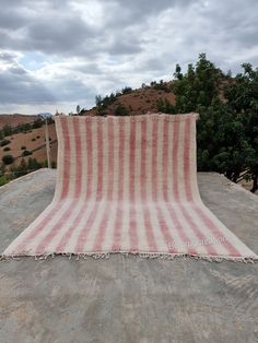 a blanket laying on top of a cement surface next to trees and hills in the background