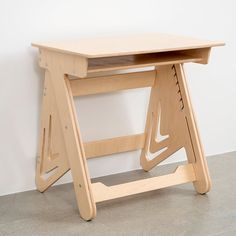 a wooden desk sitting on top of a floor next to a white wall with a black cat laying underneath it