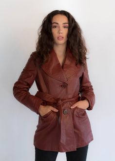 "Vintage 70s belted leather coat. The stand out on this bohemian classic is the oversized collar, buttons, and back pleated stitch detail. Wide wing collar. Long sleeves with wide cuffs. Front pockets. Front sash belt. Back waist panel with stitch detail. Large front button fastening. Fully lined. We kindly ask that you please view all measurements for comparison so you can get your desired fit. * Brand: Junior Gallery * Decade: 1970s * Fabric: 100% Leather * Lining: Satin * Color: Rustic Red C Retro Belted Fall Outerwear, Retro Belted Outerwear For Fall, Vintage Red Leather Outerwear, Vintage Leather Outerwear For Fall, Vintage Long Leather Jacket For Fall, Retro Leather Outerwear For Fall, Brown Vintage Outerwear For Fall, Brown Vintage Fashion Outerwear For Fall, Brown Outerwear For Fall Vintage Fashion