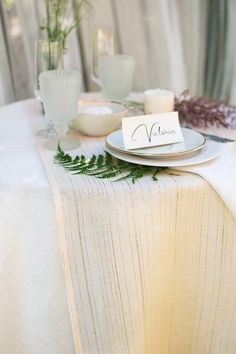 the table is set with place cards, silverware and greenery for an elegant dinner