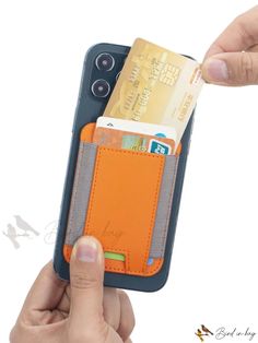 a person holding an orange and gray wallet with credit cards sticking out of the pocket