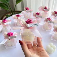 a hand holding a small glass box filled with white and pink flowers on top of a table