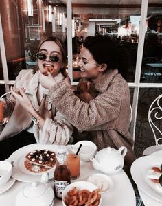 two women sitting at a table with plates of food and drinks in front of them