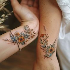 two women with matching tattoos on their arm and wrist, both holding each other's hands