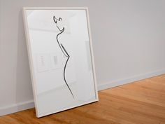 a white framed art piece sitting on top of a hard wood floor next to a wall