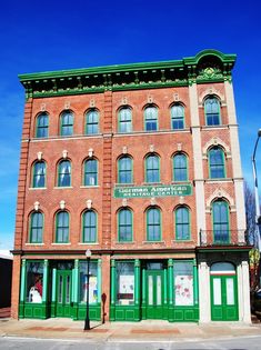 an old brick building with green doors on the front and side windows is shown against a blue sky