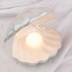 a white shell shaped candle holder with a light inside it on a white cloth background