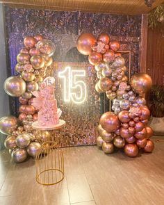 a table topped with a pink cake surrounded by lots of gold and silver balloons that spell the number fifteen