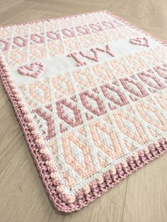 a pink and white crocheted rug with the words love written across it on a wooden floor