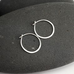 "These tiny silver hoops are shaped out of sterling silver or 14K white gold and hammered until they shimmer and shine. I wanted to make a simple hoop that would be perfect for wearing daily and would be so comfortable that you could forget that you're even wearing them. The posts are tuck into a loop catch on the backside of the earring. This particular pair of earrings from the line is a tiny circle - about 3/4\". Made from responsible and recycled metals - sterling silver and 14K white gold. Minimalist Hoop Earrings With Sterling Silver Clasp As Gift, Minimalist Hoop Earrings With Sterling Silver Clasp, Minimalist Hammered Huggie Jewelry, Silver Dainty Hammered Hoop Earrings, Dainty Hammered Silver Hoop Earrings, Minimalist Hammered Sterling Silver Hoop Earrings, Everyday Sterling Silver Hammered Hoop Earrings, Everyday Handmade White Gold Hoop Earrings, Minimalist Hammered Hoop Earrings For Anniversary