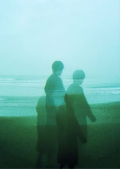 two people walking on the beach in front of the ocean