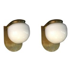 two light wall sconces with white glass balls mounted on brass metal brackets against a white background