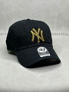 This is a black New York Clean Up adjustable hat that is hand embellished with translucent gold Swarovski crystals on the front logo. This hat features over 150+ Swarovski crystals. - 100% Cotton - Matching fabric strap & buckle - One Size Fits All - Raised Embroidered Logo - 150+ Swarovski gold crystals individually placed by hand - Ready to ship in 1 week from San Diego, CA Gold Baseball Cap For Streetwear, Gold Adjustable Hats With Rhinestones, Adjustable Gold Hat With Rhinestones, Gold Snapback Hat One Size, Gold Adjustable Cap, Adjustable Gold Cap, Gold Flat Brim Hat, One Size Fits Most, Gold Flat Brim Hat One Size, Black Snapback Baseball Cap For Party