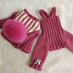 two knitted mittens and gloves laying on a white sheet with a pink pom - pom