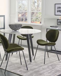 a white table with four green chairs in front of a window and rug on the floor