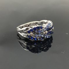 14K Sapphire and Diamond Band METAL: 14K White Gold TOTAL WEIGHT: DIAMONDS: 4 Round Brilliant Diamonds COLOR: G/H CLARITY: VS2 TOTAL WEIGHT: 0.04 ct GEMSTONES: Round brilliant cut blue sapphires TOTAL WEIGHT: 1.22 ct SIZE: Ladies size 5-8. Please indicate your ring size at checkout. DESCRIPTION: This gorgeous ring has a braided design of light and dark blue sapphires. It has four small bezel set diamonds in between each braid. It is 8.5mm wide with a 3mm height. The shank tapers down to 3mm. FRE Anniversary Multi-stone Sapphire Ring In White Gold, Anniversary Cluster Sapphire Ring In Fine Jewelry Style, Anniversary White Gold Multi-stone Sapphire Ring, Fine Jewelry White Gold Sapphire Cluster Ring, Fine Jewelry Sapphire Cluster Ring For Anniversary, Anniversary Cluster Sapphire Ring, Anniversary Sapphire Cluster Ring, Fine Jewelry Multi-stone Sapphire Ring In 14k White Gold, Exquisite Multi-stone Sapphire Ring In White Gold