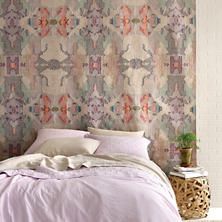 a bed with pink sheets and pillows in front of a colorful wallpaper