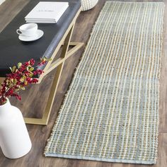 a table with a vase on top of it next to a rug and coffee cup