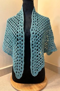 a blue crocheted shawl is on a mannequin with a black base