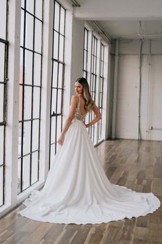 a woman in a white wedding dress standing on a wooden floor next to large windows