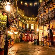 an empty city street at night with lights strung from the buildings and balconies