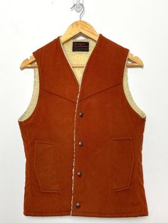 This vest has a few small marks on the back side and slight piling along the sherpa lining. (see last two photos for flaws) Measurements  Pit to pit: 17 inches  Top to bottom: 24 inches Rugged Brown Vest Outerwear, Brown Rugged Vest For Winter, Rugged Brown Winter Vest, Brown Rugged Winter Vest, Brown Buttoned Vest For Winter, Brown Winter Vest With Buttons, Classic Winter Vest With Snap Buttons, Vintage Winter Vest Outerwear, Vintage Winter Vest With Button Closure