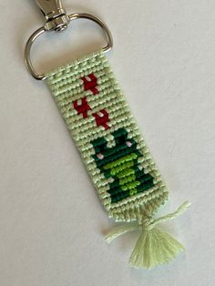 a key chain with a green and red cross stitched design on it, hanging from a metal hook