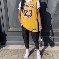 a young person wearing a lakers jersey and holding a baseball glove standing in front of a building