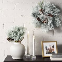 two white vases with pine cones and candles on a table next to a brick wall