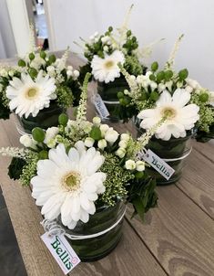 white flowers are arranged in small glass vases on a wooden table with price tags