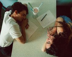 two people sitting at a table with notebooks and papers in front of their faces