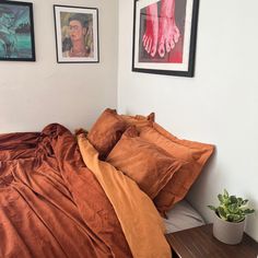 a bed with two pictures on the wall above it and an orange comforter set