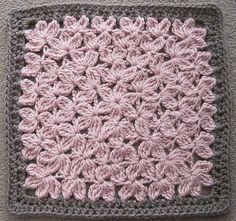 a crocheted square with pink and gray flowers on the center is sitting on a carpet