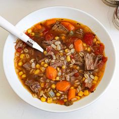 a white bowl filled with corn and beef soup next to a jar of silverware