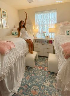 a woman sitting on top of two beds in a room with white furniture and pink pillows