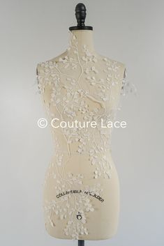 a mannequin with white flowers on it's torso and neckline, in front of a gray background