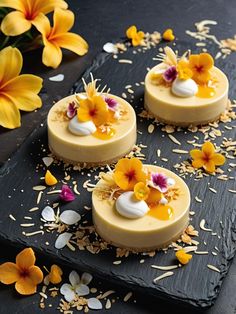 three desserts are sitting on a black tray with flowers and petals scattered around them