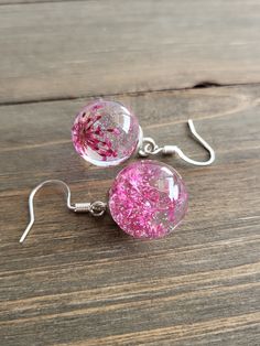 Beautifully Rose Pink flower earrings, elegant glass orb earrings with delicate, dried flowers inside. Solid glass ball earrings have silver finishing and hooks. The color of rose symbolizes courage, passion, and joy.  In earlier centuries, a gift of flowers was a meaningful gesture meant to portray the surrounding feelings involved, and show deep affection and appreciation for the receiver. It was known, Rose Pink was worn as a representation of luxury and wealth, as it was an expensive color worn by the upper class of society by privileged women of high stature. A gift of blushing rose pink flower earrings, complimented with gold, will surely bring a smile to her face. These burning pink~red floral earrings offer to be the most brilliant and unique jewelry piece in her jewelry box. Pink Silver Sterling Flower Earrings With Pressed Flowers, Silver Round Resin Earrings, Silver Sterling Silver Earrings With Pressed Flowers, Pink Flower Glass Jewelry, Pink Flower-shaped Glass Jewelry, Silver Pressed Flower Earrings, Elegant Silver Earrings With Pressed Flowers, Clear Round Sterling Silver Earrings, Silver Pressed Flower Resin Earrings