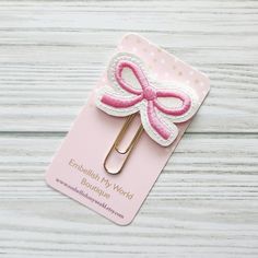 a pink and white bow clip on top of a wooden table next to a card