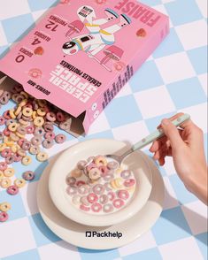 a person is eating cereal from a bowl on a table next to a pink box