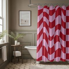 a red and white shower curtain sitting next to a bath tub in a bathroom under a window