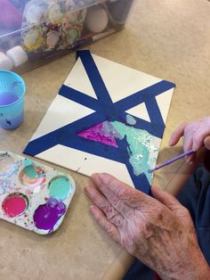 an older woman is painting on a piece of paper