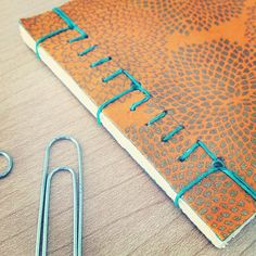 an orange and blue notebook sitting on top of a wooden table next to a pair of scissors