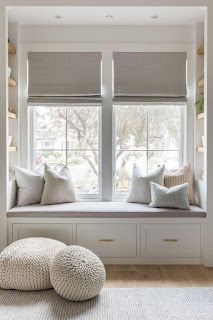 a window seat with two pillows on it in front of the windowsill and some shelves