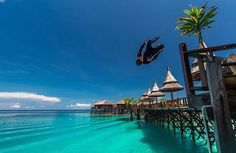 a person jumping into the water from a dock with thatched umbrellas on it