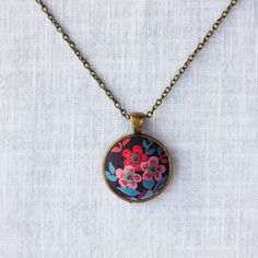 Inspired by Liberty Art Fabric, I developed my collection of vintage-style jewellery. The vibrant floral motifs of Liberty fabric are truly celebrated and showcased in this collection. A great gift for nature-lovers that will never go out of fashion. This necklace features red flowers in a dark background. It has an antique bronze alloy pendant tray and an oval pendant. The long brass chain has a lobster clasp and a tiny bee beside it. Pendant 2.8 x 2.8 cm Handmade in my studio based in England. Artistic Flower Pendant Necklaces For Gifts, Bohemian Flower-shaped Nickel Free Necklace, Bohemian Flower-shaped Nickel-free Necklace, Artistic Flower Pendant Jewelry Gift, Multicolor Retro Jewelry For Vintage Collection, Retro Handmade Flower Jewelry, Bohemian Necklace With Round Flower Charm Pendant, Adjustable Vintage Necklace As Gift, Vintage Necklaces With Pressed Flowers For Jewelry Making