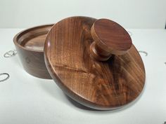 a wooden container with a lid on a white tableclothed surface, next to two silver rings