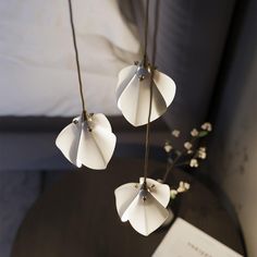 three white flowers are hanging from the ceiling in front of a book on a table