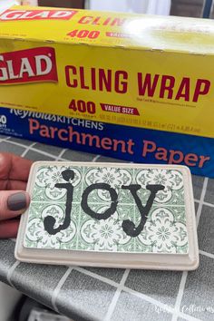 a person holding a piece of paper with the word joy on it and a box of glue